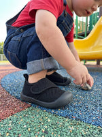 Kleinkind spielt draußen mit Babyloom Puschies Schwarz Barfußschuhen